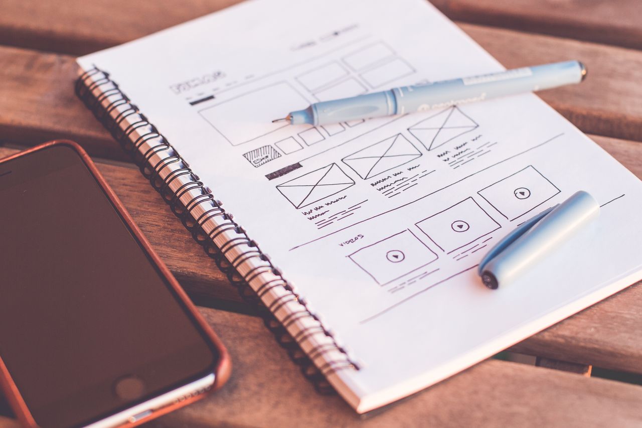 Crafting Captivating Headlines: Your awesome post title goes here Close-up of a notebook with wireframe sketches and a smartphone on a wooden desk.