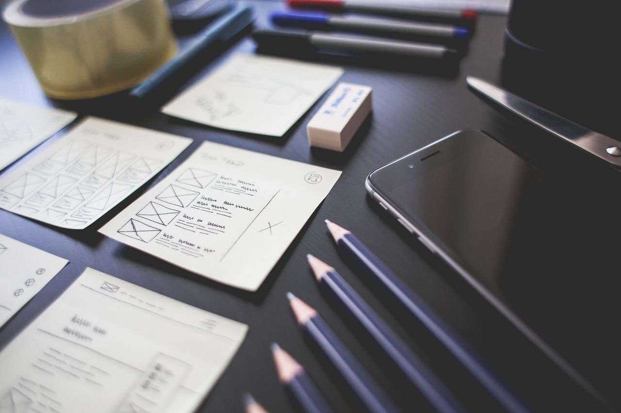 Offerings A creative workspace featuring UI design plans, pencils, a smartphone, and other office tools.