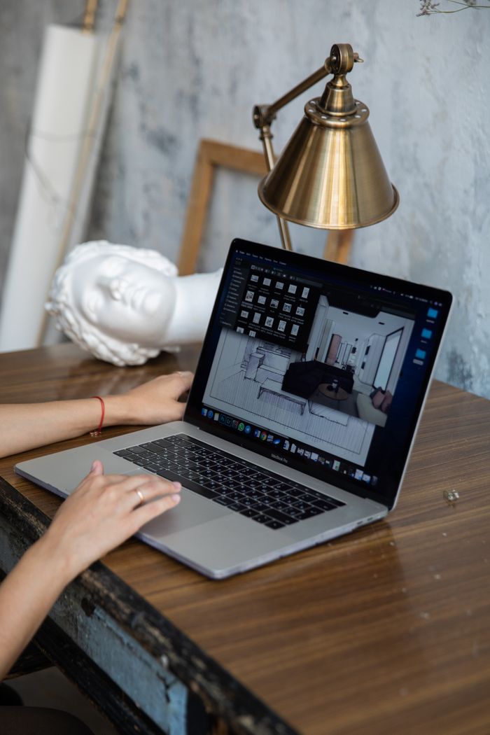 Portfolio A person working with interior design software on a laptop at a desk with a lamp and statue.